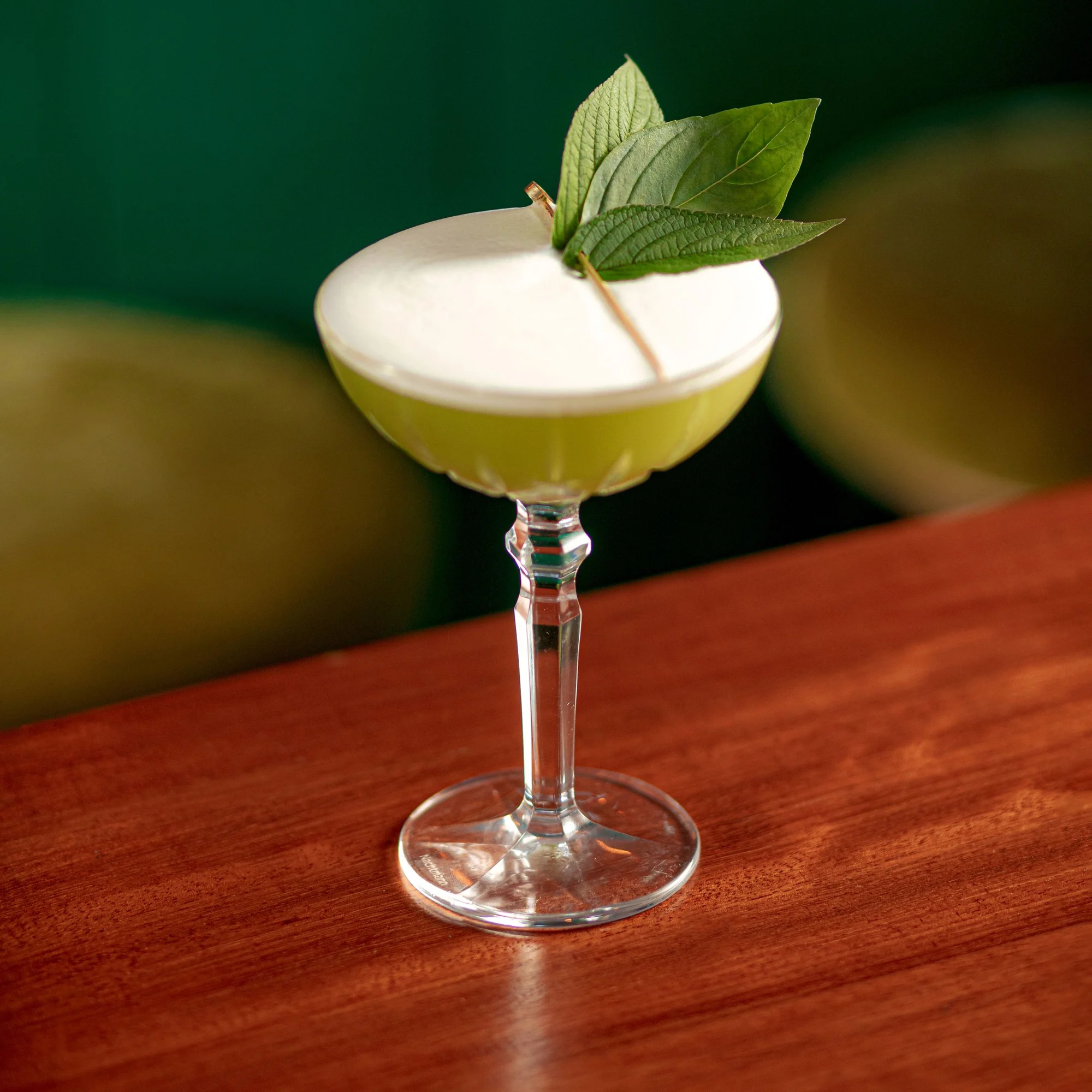 A pale green Ate cocktail in a coupe, finished with fresh leaves